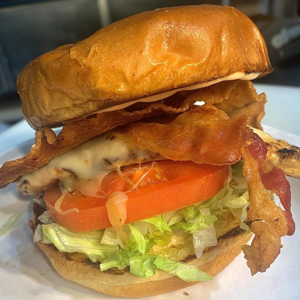 A close-up of a Cafe772 Cantina & Grill burger with bacon, melted cheese, tomato, and lettuce.