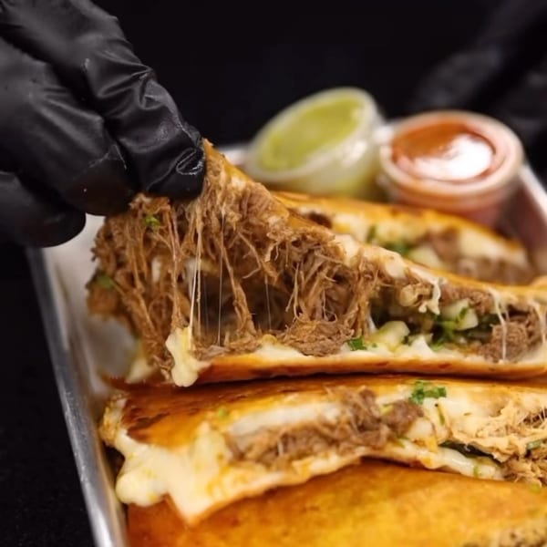 Gloved hand pulling apart a Cafe772 Cantina & Grill quesadilla, showing melted cheese and shredded meat.