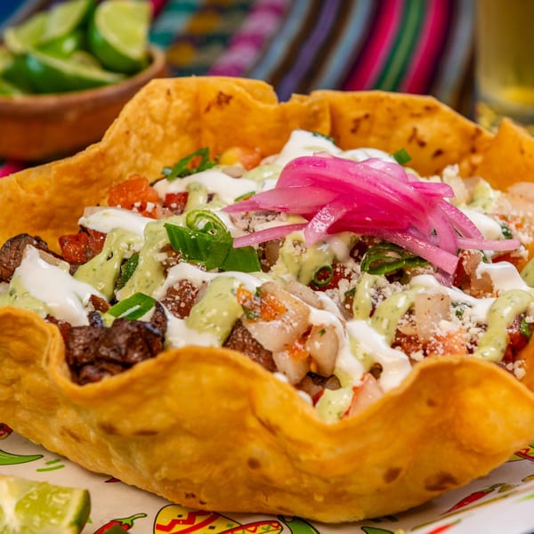 A crispy taco salad bowl filled with meat, pico de gallo, sauces, and pickled red onions.